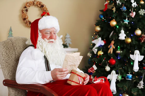 Santa Claus sitting with children letters in comfortable chair near fireplace at home Stock Photo