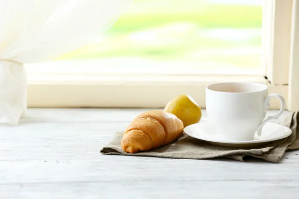 Sabroso croissant y la taza del té en la servilleta sobre el fondo claro — Foto de Stock