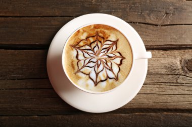 Bir fincan latte sanat kahvesi, ahşap masa, üst manzara.