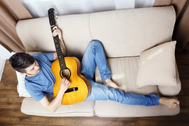 Odadaki kanepede gitarlı genç adam.