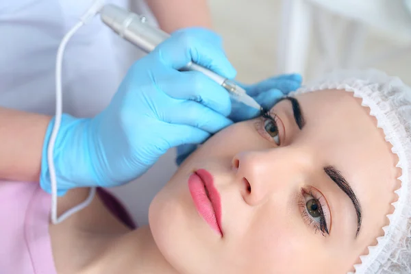 Cosmetologist applying permanent make up on eyes, close-up