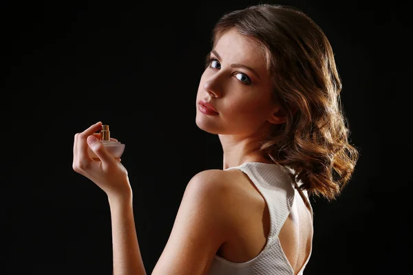 Vacker kvinna med parfymflaska på svart bakgrund — Stockfoto