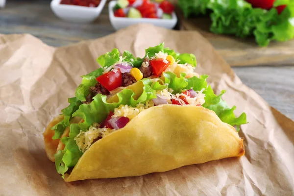 Taco saboroso com legumes em papel na mesa close-up — Fotografia de Stock