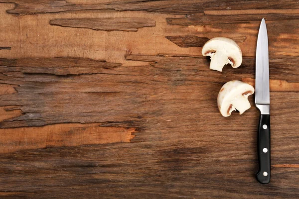 Halves of mushroom with knife on wooden background — Stock Photo, Image
