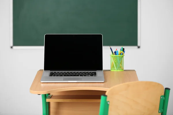 Wooden desk with stationery and laptop in class on blackboard background — Stock Photo, Image