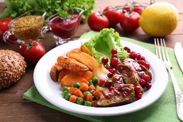 Beef with cranberry sauce, roasted potato slices, vegetables on plate, on  wooden background — Stock Photo, Image