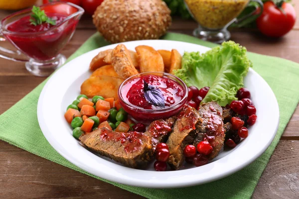 Beef with cranberry sauce, roasted potato slices, vegetables on plate, on  wooden background — Stock Photo, Image