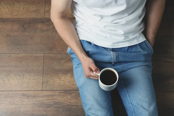 Joven sentado en el suelo con una taza de café en la habitación —  Fotos de Stock