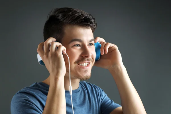 Knappe jongeman, luisteren naar muziek op een grijze achtergrond — Stockfoto