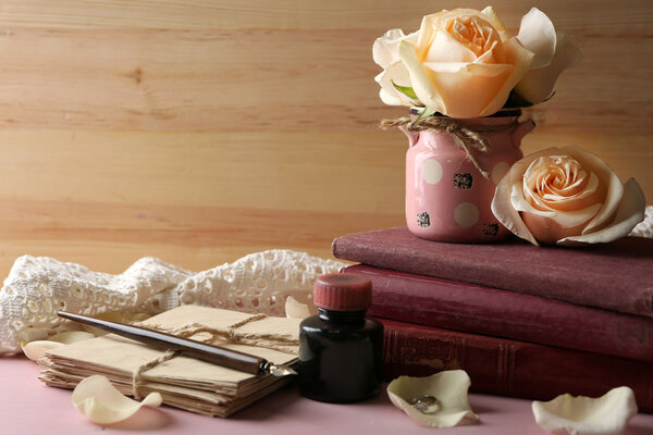 Цветок розы со старой книгой и буквами на цветном деревянном фоне стола. Винтажная концепция
