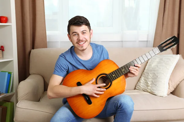 Joven con la guitarra en el sofá en la habitación —  Fotos de Stock