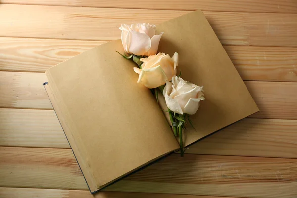 Fresh roses on old notebook, on wooden table background — Stock Photo, Image