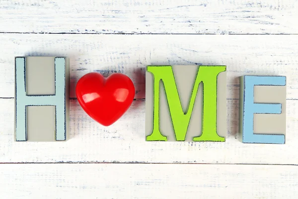 Decorative letters forming word HOME with decorative heart on wooden background — Stock Photo, Image