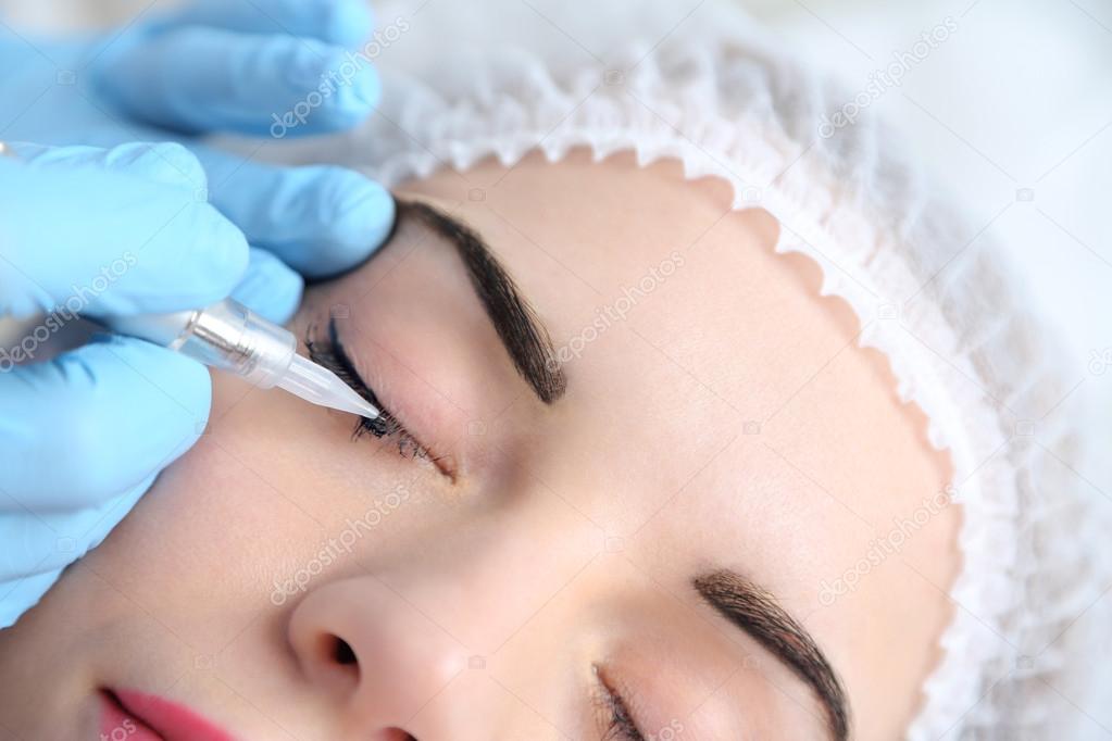 Cosmetologist applying permanent make up on eyes, close-up