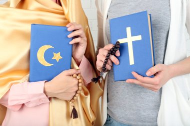 Two friends holding books with religions symbols