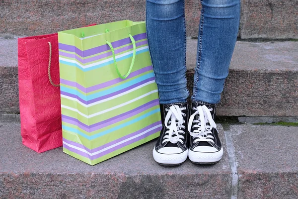 Vrouwelijke voeten in gumshoes in de buurt van shopping bag op stenen trappen — Stockfoto