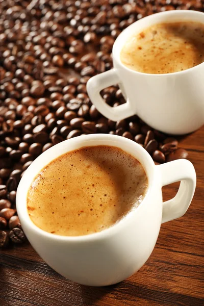 Duas xícaras de café fresco com grãos na mesa, close-up — Fotografia de Stock