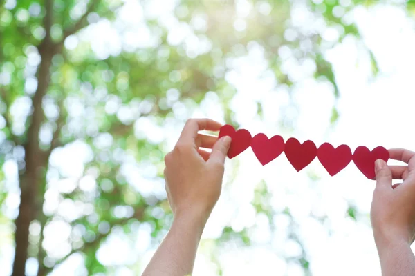 Женские руки с цепью бумажных сердец на фоне природы — стоковое фото