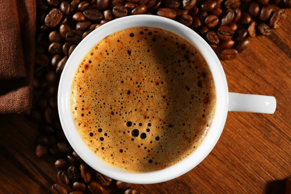 Tasse frischen Kaffee mit Bohnen auf dem Tisch, Nahaufnahme — Stockfoto