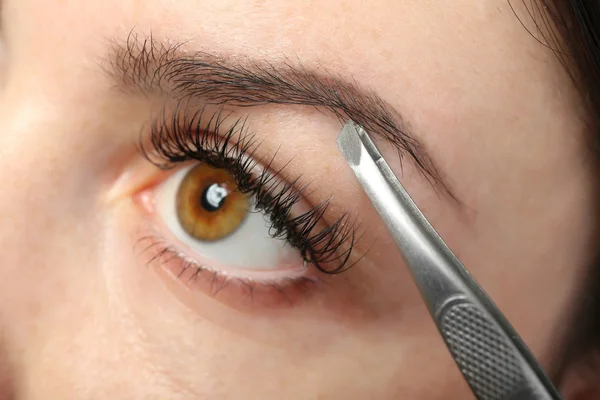 Mujer joven arrancando las cejas con pinzas de cerca — Foto de Stock