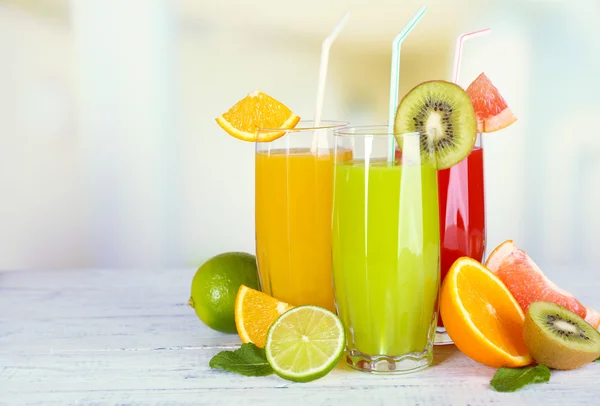 Vasos de diferentes jugos con frutas y menta sobre fondo brillante — Foto de Stock