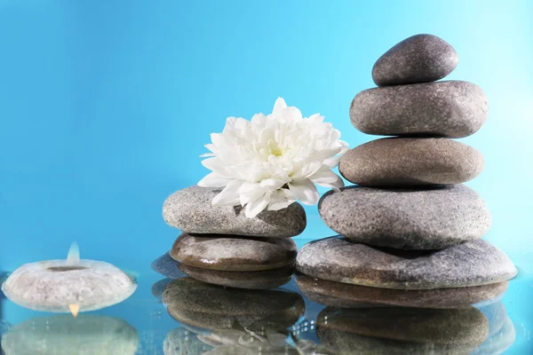 Stack of spa stones with flower and candlelight on blue background — Stock Photo, Image