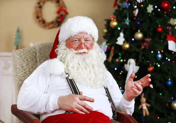 Санта-Клаус сидит в удобном кресле у камина дома — стоковое фото