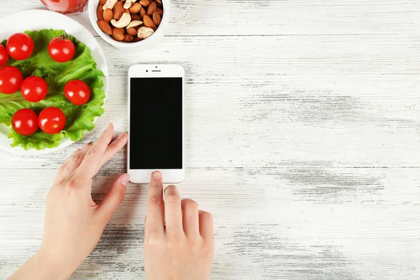 Mat och mobiltelefon i kvinnliga händer — Stockfoto