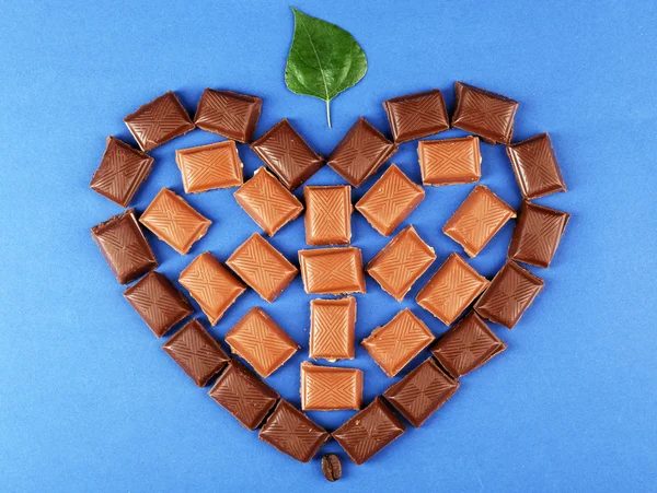 Chocolate pieces arranged in heart shape with green leaf — Stock Photo, Image