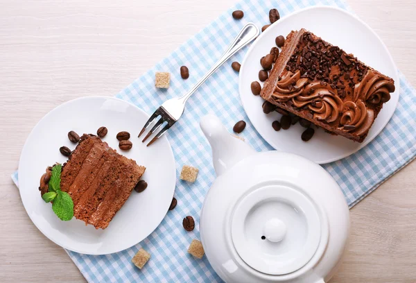 Tasty pieces of chocolate cake with lump sugar and coffee beans near teapot on wooden table background — Stock Photo, Image