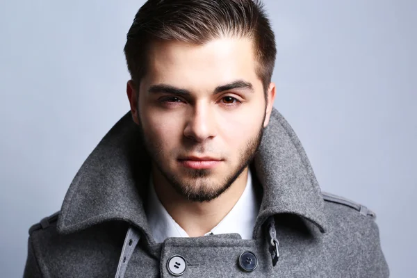 Young man in coat on gray background — Stock Photo, Image