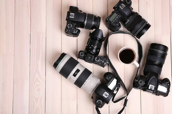Modern cameras and cup of coffee on wooden table, top view — Stock Photo, Image