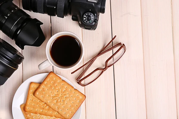 Modern cameras with glasses, cup of coffee and cookies on wooden table, top view — Stock Photo, Image