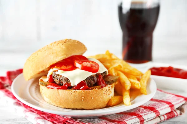 เบอร์เกอร์อร่อยกับเฟรนช์ฟรายบนจาน บนพื้นหลังโต๊ะไม้ ความคิดเกี่ยวกับอาหารที่ไม่ดีต่อสุขภาพ — ภาพถ่ายสต็อก