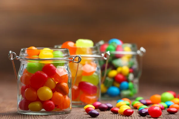 Красочные конфеты в банках на столе на деревянном фоне — стоковое фото