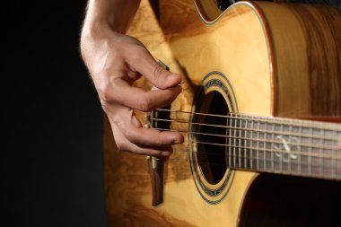 Genç adam akustik gitarla karanlık arka planda çalıyor.