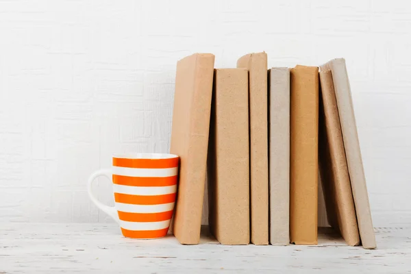 Boeken en cup op houten plank op wallpaper achtergrond — Stockfoto