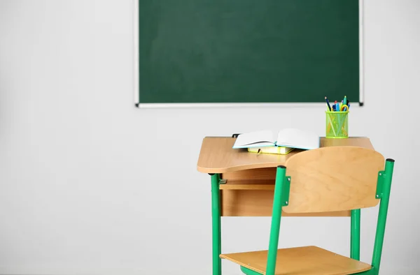 Mesa de madeira com artigos de papelaria e cadeira em sala de aula sobre fundo quadro-negro — Fotografia de Stock