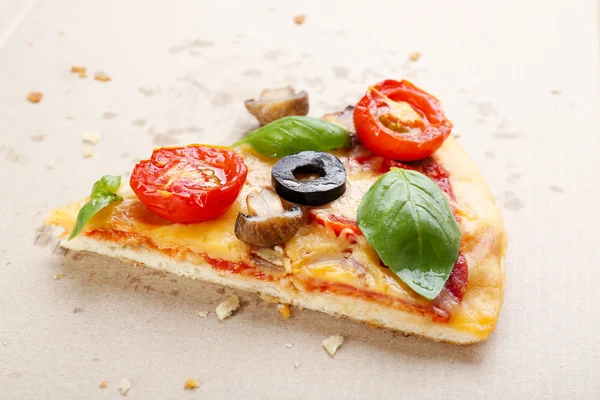 Slice of tasty pizza with vegetables and basil in cardboard box close up — Stock Photo, Image