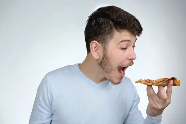 Ung man äta bit pizza på grå bakgrund — Stockfoto