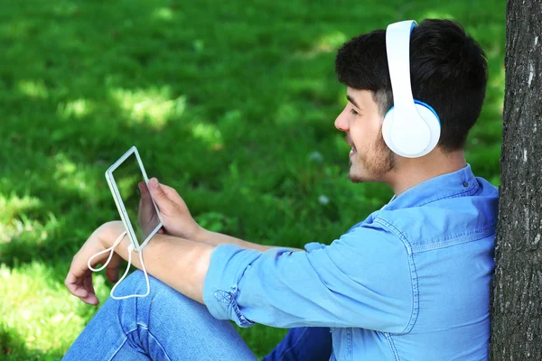 Hombre con auriculares descansando bajo el árbol en el parque —  Fotos de Stock