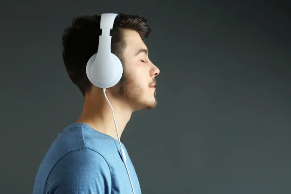 Handsome young man listening to music on grey background — Stock Photo, Image