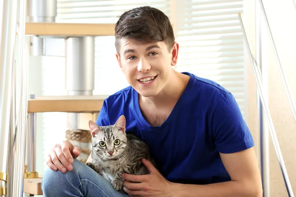 Handsome young man with cute cat sitting on steps at home — Stock Photo, Image