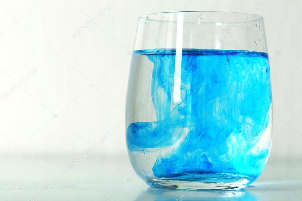 Glass of water with blue paint on table close up