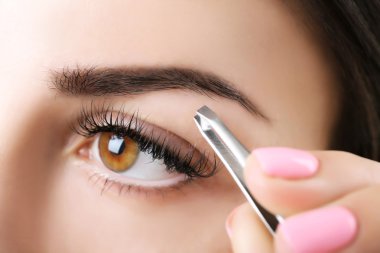 Young woman plucking eyebrows with tweezers close up clipart