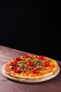 kiraz domates, yeşil zeytin ve siyah arka plan üzerine ahşap masa üzerinde otlar ile lezzetli pizza