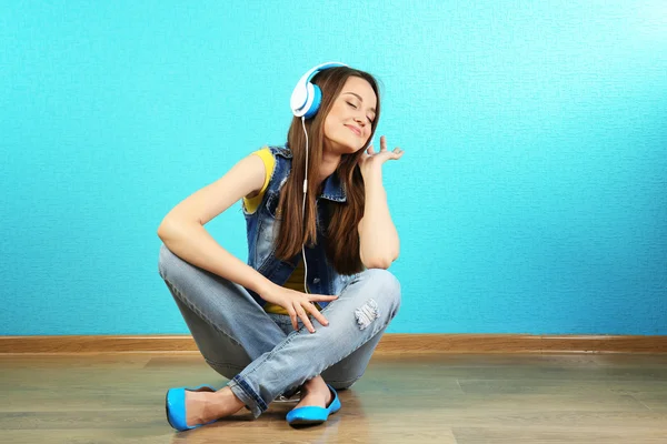 Mladá žena, sedící na podlaze se sluchátky na tyrkysové tapety pozadí — Stock fotografie