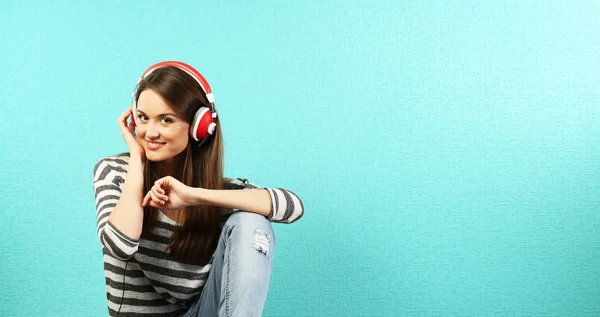 Young woman sitting on floor with headphones on turquoise wallpaper background — Stock Photo, Image