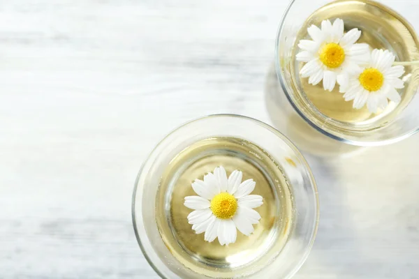 Glasses of chamomile tea with chamomile flowers on color wooden background — Stock Photo, Image