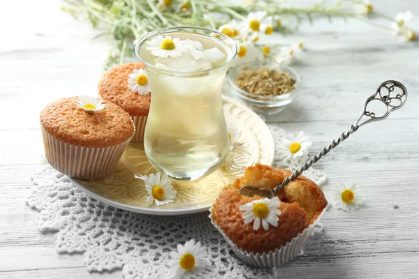 Bicchiere di tè alla camomilla con fiori di camomilla e gustosi muffin su sfondo di legno di colore — Foto Stock